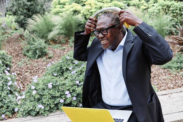 IMAGO Creative: Klimawandel - Zukunft und Innovation Smiling businessman wearing headphones while sitting with laptop on bench model released Symbolfoto ASGF00926