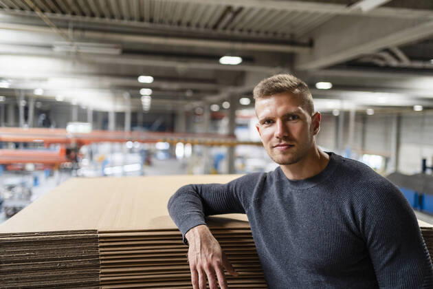 IMAGO Creative: Business, Inflation und Lieferketten Young businessman staring while leaning on cardboard stack model released Symbolfoto property released DIGF16209