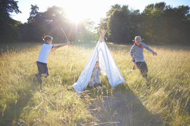IMAGO Creative, Jahreszeit Sommer, Sommerferien Small group of young boys playing around teepee, 31.07.2014, Copyright: xPeterxMullerx, model released, aiming,attacking,chasing,running,hiding,holding,playing,dressing up,pretending,differential focus,full length,striped,adolescence,adventure,childhood,concentration,escape,serious,adrenaline,carefree,competition,fun,innocence,safety,teamwork,togetherness,friendship,happiness,nature,grass,toy,toy gun,weapon,child,12 to 13 years,only children,male,boy,only boys,pre-adolescent boy,three people,cowboy,teepee,outdoors,park,field landscape,summer,day,casual clothing,costume,cowboy hat,laughing,smiling,sunlight,bow and arrow,make believe,13 to 14 years,native american,indian,long grass,field,only male,role playing,native american costume,8 to Ref:IS09AJ66A