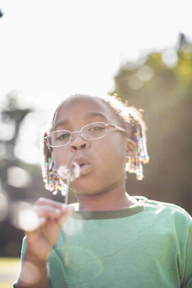 IMAGO Creative: Klimawandel - Umwelterziehung Portrait of girl blowing dandelion clock in parkland eco camp, 01.09.2014, Copyright: xChadxSpringerx, model released, wearing,learning,holding,camping,looking at camera,looking up,green color,copy space,differential focus,front view,head and shoulders,portrait,childhood,responsibility,harmony,innocence,well being,happiness,hope,nature,child,african american ethnicity,female,girl,only one girl,one person,outdoors,rural,summer,day,casual clothing,eyeglasses,t-shirt,education,environmental issue,environmental conservation,blowing,lifestyle,leisure,5 to 6 years,only female,dandelion clock,dandelion seed,parkland,September 2014 Release,Blowing,Thinking,Learning,Holding,Looking Up,Camping,African Descent,African American Ethnicity,Child,Eleme Ref:IS09AK90X