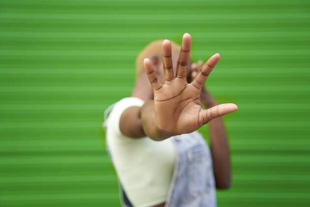 Young woman gesturing stop sign in front of green wall model released Symbolfoto VEGF04872