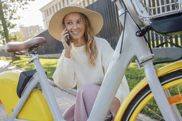 IMAGO Creative: Klimawandel - Zukunft und Innovation Smiling blond woman talking on smart phone while crouching by bicycle model released Symbolfoto VPIF04854
