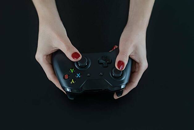 IMAGO Creative, Lifestyle, Gaming Top view of woman hands with red nail polish on fingers holding a logo free modern gaming controller for playing digital video games isolated on black for fun leisure entertainment, 13.10.2020, Copyright: xAngelicaCorneliussenx Panthermedia26575592