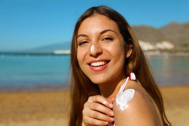 IMAGO Creative, Jahreszeit Sommer, Sonnenschutz Beautiful happy cute woman applying suntan cream to her nose and shoulder with beach background model released, Symbolfoto, 13.10.2020, Copyright: xsergiomontix Panthermedia27230752