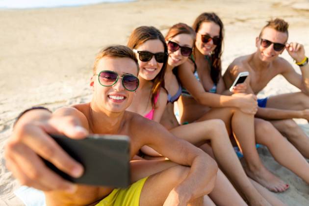 IMAGO Creative, Jahreszeit Sommer, Sommerferien friendship, leisure, summer, technology and people concept - friends sitting and taking selfie with smartphone on beach Copyright: xlevxdolgachovx 18901714
