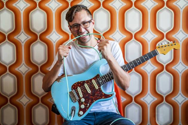 Young male guitarist biting guitar cable in front of wall model released Symbolfoto property released DLTSF02242