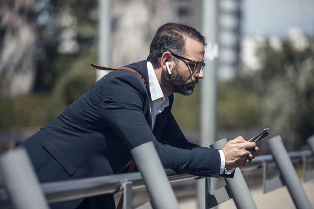 Male business professional using mobile phone while leaning on railing model released Symbolfoto JSRF01654