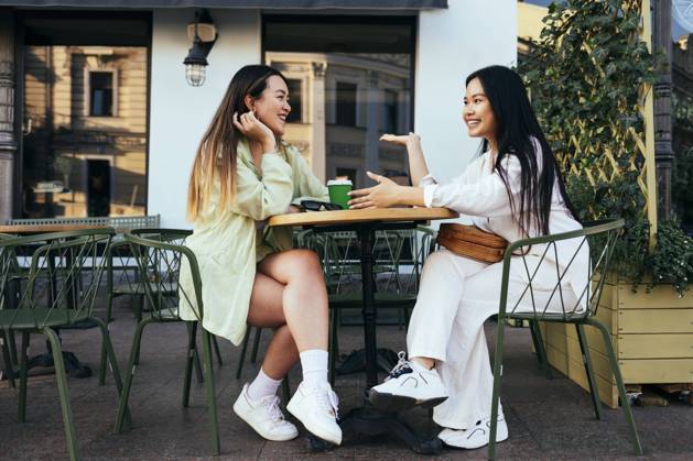 Smiling female friends talking at sidewalk cafe model released Symbolfoto OYF00539