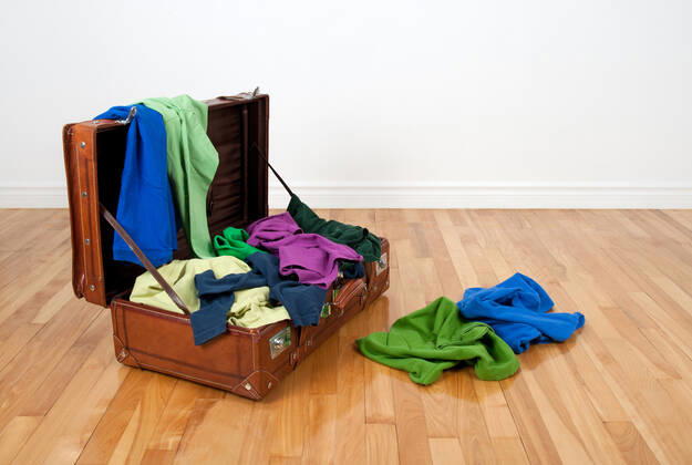 Leather suitcase on a wooden floor in an empty room, full of colorful clothing. Copyright: xx 5404288