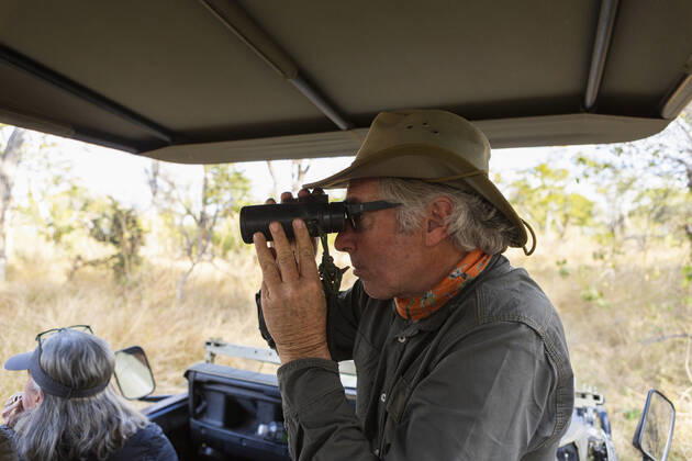 Safari guide using binoculars in a jeep with a family Okavango Delta,Botswana,Safari guide using binoculars in a jeep with a family  Safari guide using binoculars in a jeep with a family