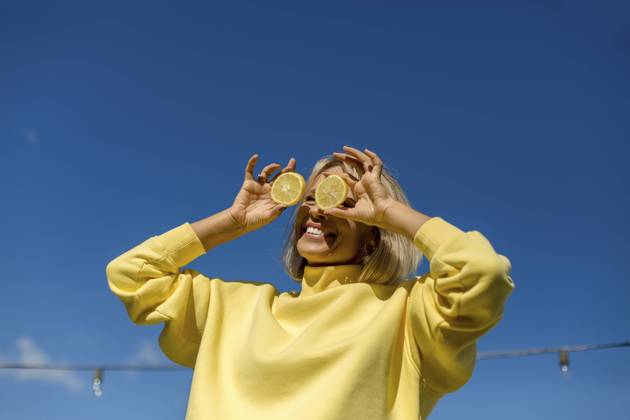 Cheerful woman holding slice of lemon in front of eyes during sunny day model released, LLUF00168