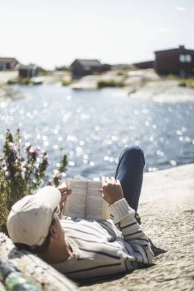 IMAGO Creative, Jahreszeit Sommer, Sommerferien Man reading book while lying down on rock during sunny day Sweden, Stockholm archipelago, model released Copyright: xMaskotx , MA90592