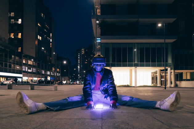 IMAGO Creative: 2022 Aussichten Italy, Woman withÃäVR goggles sitting on sidewalk in city at night Italy, Woman withÃäVR goggles sitting on sidewalk in city at night