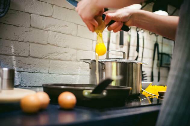  woman housewife prepares fried eggs with ham and vegetables in his kitchen. egg breaks, adding to the pan model released, Symbolfoto, 25.09.2021, Copyright: xevgeniykleymenovx Panthermedia23845358