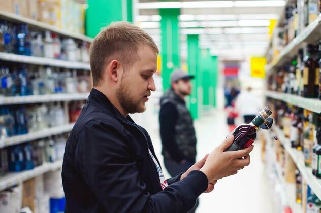 IMAGO Creative: Business, Inflation und Lieferketten bearded man, In a black jacket, stopped to make my choice in store window, holds a bottle of strong alcohol in his hand, taking from shelf model released, Symbolfoto, 26.09.2021, Copyright: xevgeniykleymenovx Panthermedia23930306