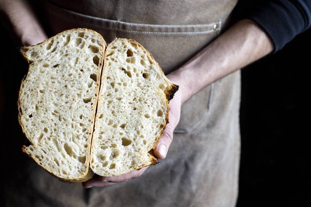 Baker holding halved loaf of bread at bakery model released property released, IFRF01296