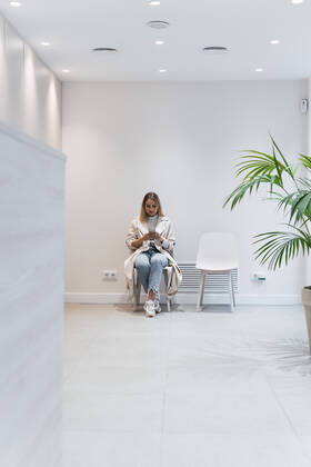 Woman using smart phone sitting in waiting room at clinic model released property released, PNAF03062