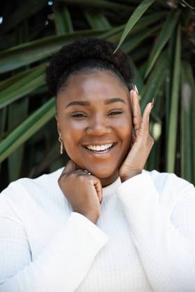 Creative Highlights Symbolbilder Positive African American female touching cheek while standing near lush green plants on summer day in garden DaniNavarro_BlackWoman_21.jpg Copyright: xDanixNavarrox Model Released