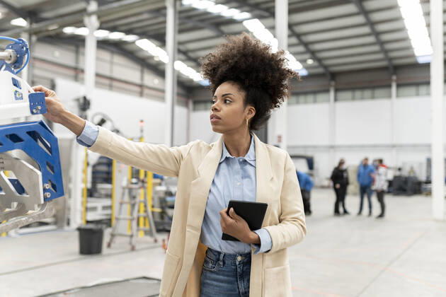 IMAGO Creative: Business, Inflation und Lieferketten Businesswoman holding tablet PC analyzing machine in factory model released property released, JCCMF05593
