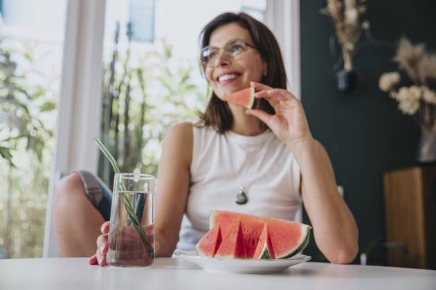 Woman sitting at home holding drinking glass by watermelon slice on table model released property released, MFF08845