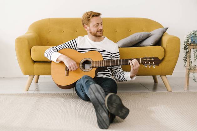 Young man playing guitar sitting in front of sofa at home model released property released, XLGF02886
