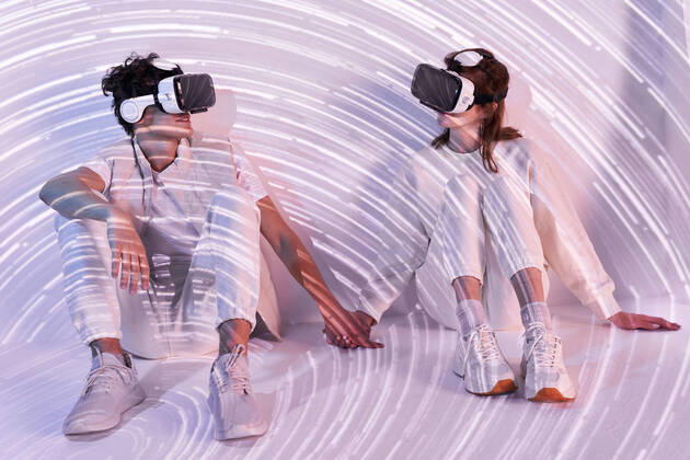IMAGO Creative: Business, Innovative Technologie-L?sungen Full body of couple in modern VR goggles exploring virtual reality while sitting at wall holding hands with long exposure lights in studio ManuelRuiz_VRCouple_4.jpg Copyright: xManuelxRuizx Model Released