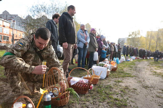 BUCHA, UKRAINE - APRIL 24, 2022 - A serviceman sits on his haunches near an Easter basket before a consecration ceremony outside the Church of Saint Andrew the First-Called Apostle during the Orthodox Easter celebration in Bucha that is recovering from the war crimes committed by Russian troops after its liberation from Russian invaders, Kyiv Region, northern Ukraine. Easter service in Bucha  Copyright: xHennadiixMinchenkox
