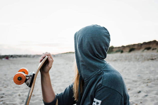 IMAGO Creative: Sommer Sport - Strand woman with her hood up at the beach holding skateboard at sunset Christchurch, England, United Kingdom CR_RABE210920-830236-01 ,model released, Symbolfoto