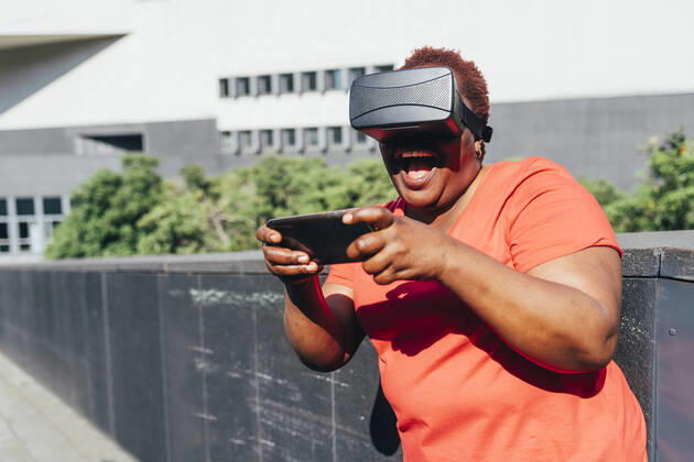 IMAGO Creative: Business, Innovative Technologie-Lösungen Happy woman wearing virtual reality simulator using smart phone on sunny day model released, Symbolfoto, MEUF05489