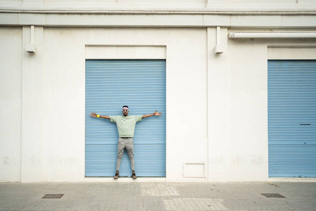 Young man standing with arms outstretched in front of blue shutter model released, Symbolfoto, RCPF01453