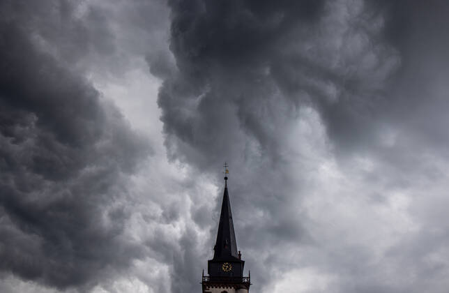 Dark clouds over the church tower Dark clouds of a shower are seen in the evening in the sky above the steeple of the Catholic Church St Ursula in Oberursel , Oberursel Hesse Germany