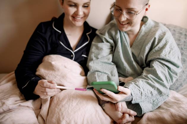 IMAGO Creative: Business, Innovative Technologie-Lösungen Happy lesbian couple checking pregnancy test results with smart phone while sitting on bed at home Sweden, Stockholm, model released, property released Copyright: xMaskotx , MA94148