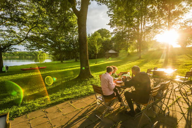 People sitting in the evening sun at a table of a garden restaurant and eating, Bavaria, Germany garden restaurant at a lakea small lake