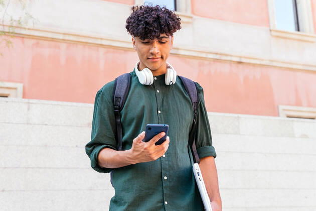 IMAGO Creative: N?chste Generation, Sozial- und klimabewusst Ethnic man with headphones looking at screen of modern mobile phone on the street DavidMunoz_FrancVilaOlimpica_00009.jpg Copyright: xDavidxMunozx Model Released