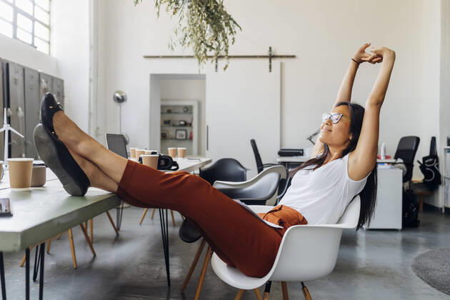Smiling businesswoman stretching arms on chair at workplace model released, Symbolfoto property released, MEUF06737