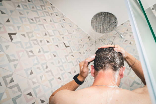 29 July 2022: attractive young man takes a shower under running water in the shower in the bathroom, body care with shampoo