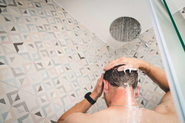29 July 2022: attractive young man takes a shower under running water in the shower in the bathroom, body care with shampoo