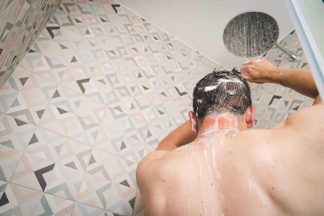 29 July 2022: attractive young man takes a shower under running water in the shower in the bathroom, body care with shampoo