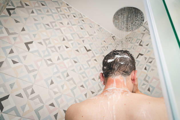 29 July 2022: attractive young man takes a shower under running water in the shower in the bathroom, body care with shampoo