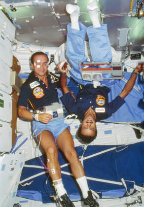 51G-102-035 (17-24 June 1985) --- The two payload specialists for the week-long flight share a middeck scene on the earth-orbiting Discovery. Sultan Salman Abdelazize Al-Saud (left) is in the midst of a meal while Patrick Baudry conducts a phase of the French Postural Experiment (FPE) on himself. Sleep restraints are in the background. Copyright: xpiemagsx piemagsspace-114945 !ACHTUNG AUFNAHMEDATUM GESCHÄTZT!