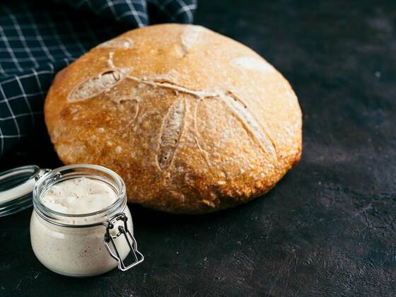 Sourdoug starter and wheat bread, copy space, Sourdoug starter and wheat sourdough bread. Wheat sour dough starter in glass jar and delicious homemade round sourdough bread on black background, copy space. Home made sourdough bread making concept, 18.05.2020 18:45:57, Copyright: xFascinadorax Panthermedia28450987.jpg