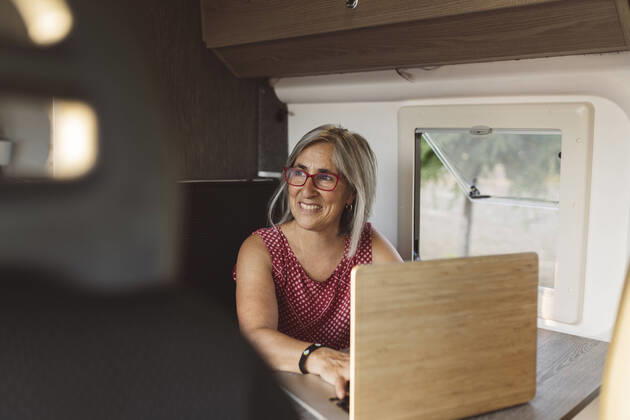 Smiling mature woman using laptop sitting in camper trailer model released, Symbolfoto, JCCMF06995