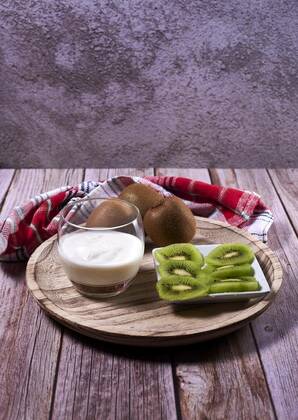  Glass with yoghurt and broken kiwis on a wooden plate, Glass with yoghurt and broken kiwis on a wooden plate. Wooden floor, whole kiwis, white and red kitchen towel, stone wall., 27.02.2021, Copyright: xRaulROFotox Panthermedia29665356.jpg