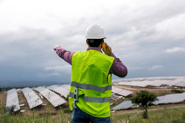 IMAGO Creative: Business, Innovative Technologie-L?sungen Back view of unrecognizable male speaking on walkie talkie against solar power station and overcast gray sky, Model released SergioVictorVega_SolarPanelArchitects_26 Copyright: xSergioxVictorxVegax MR