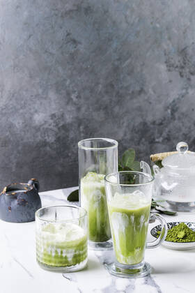Matcha iced latte Matcha green tea iced latte or cocktail in three different glasses with ice cubes, matcha powder and jug of milk on white marble table, decorated by green branches. Grey wall at background Copyright: xNatashaxBreenx NB100718-69
