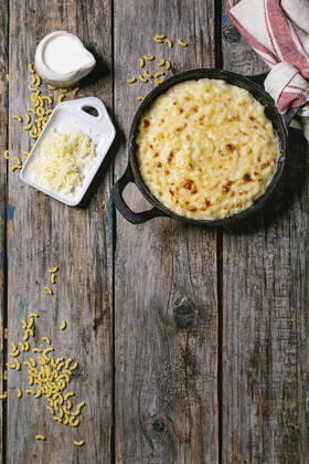 American dish mac and cheese Classic american dish baked mac and cheese in cast iron pan with kitchen towel and ingredients above over old wooden background. Flat lay, space Copyright: xNatashaxBreenx NB160919-17