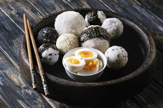 Rice balls and eggs Stone tray with different size rice balls with black sesame and seaweed nori, served with soft boiled eggs and chopsticks over wooden plank background. Asian style dinner. Copyright: xNatashaxBreenx NB161017-69