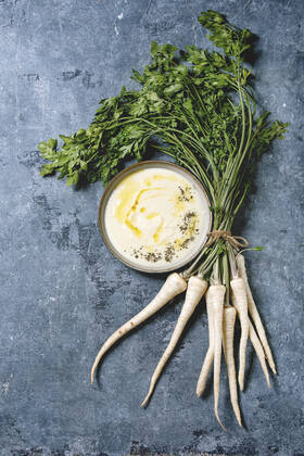 Parsnip soup with butter sauce Parsnip cream soup in ceramic bowl with butter sauce, bundle of fresh parsnip and herbs over blue texture background. Flat lay, space Copyright: xNatashaxBreenx NB300919-3