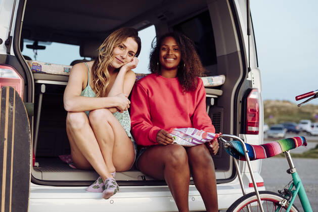 Cheerful women looking at camera while sitting on trunk of van eating popcorn, Model released ManuelRuizAlba_CamperGirls_165 Copyright: xManuelxRuizxAlbax MR