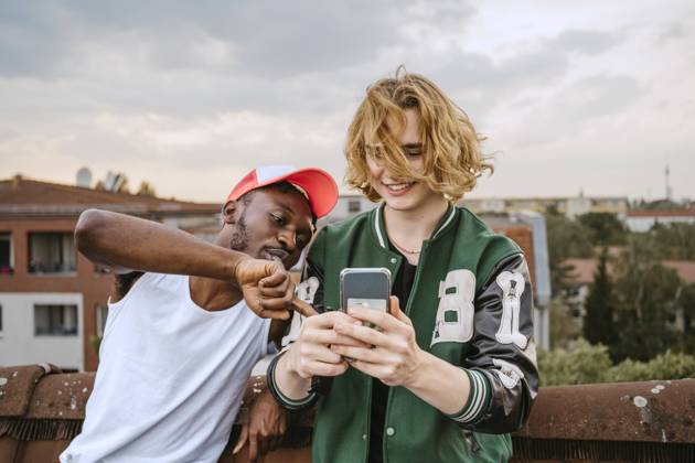 IMAGO Kreativ: Urbane Kultur - Sommer auf den Dächern IMAGO Creative: Business, Innovative Technologie-Lösungen Young man wearing hat pointing on smart phone held by male friend on rooftop Germany, Berlin, model released, property released Copyright: xMaskot,xMaskotxBildbyraxABx , MA95126 MA95126